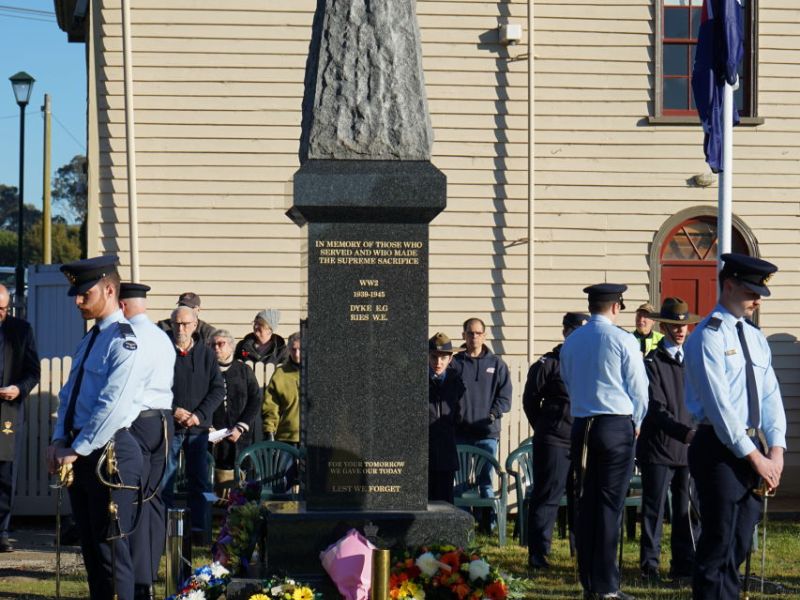 Toongabbie cenotaph in front of the historic Mechanics Hall. There are wreaths at the base of the cenotaph from the official opening and people are gathered around the area. Four members of the RAAF base East Sale are forming the catafalque party at each corner of the cenotaph. 