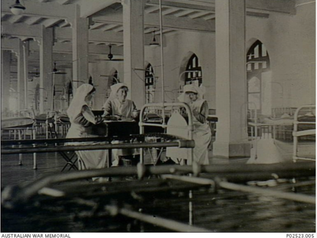Bombay, India. c 1917. Three members of the Australian Army Nursing Service (AANS) sitting at a table in a ward at Victoria War Hospital. The hospital had two hundred beds on each of the first three floors and Sister's quarters on the fourth. It received the most serious cases as it was five minutes from the dock. Patients were received from Mesopotamia, including British POWs released by the Turks, Turkish prisoners and British troops. At one stage, British troops suffering from heatstroke were received at