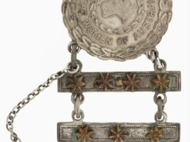 Circular white metal badge with a wreath surmounted by a King's Crown. Inside is a map of Australian surrounded by another wreath and the words 'TO THE WOMEN OF AUSTRALIA'. Two bars with a total of seven brass Federation Stars are suspended from the main body. The number of stars represents the number of relatives involved in the war effort. 