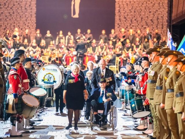 Sir Peter Cosgrove leads Des from the 2025 Anzac Tribute Sydney Opera House together with War Widow Marguerite Ryan. Photo by Giovanni Portelli
