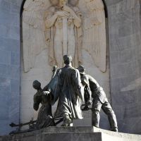 The spirit of Duty, bearing in its hands a sword shaped as a cross, the symbol of battle and sacrifice. The group in front is symbolic of the youth of the community.