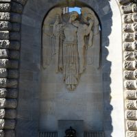 The spirit carries on its left arm the limp figure of a dead hero, while in its right hand it holds the cross-like sword, now in its scabbard.